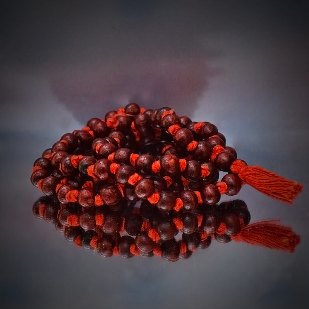 This is a picture of a "MALA" of dark red sandalwood and, each bead of red sandalwood placed on a reflective background.
