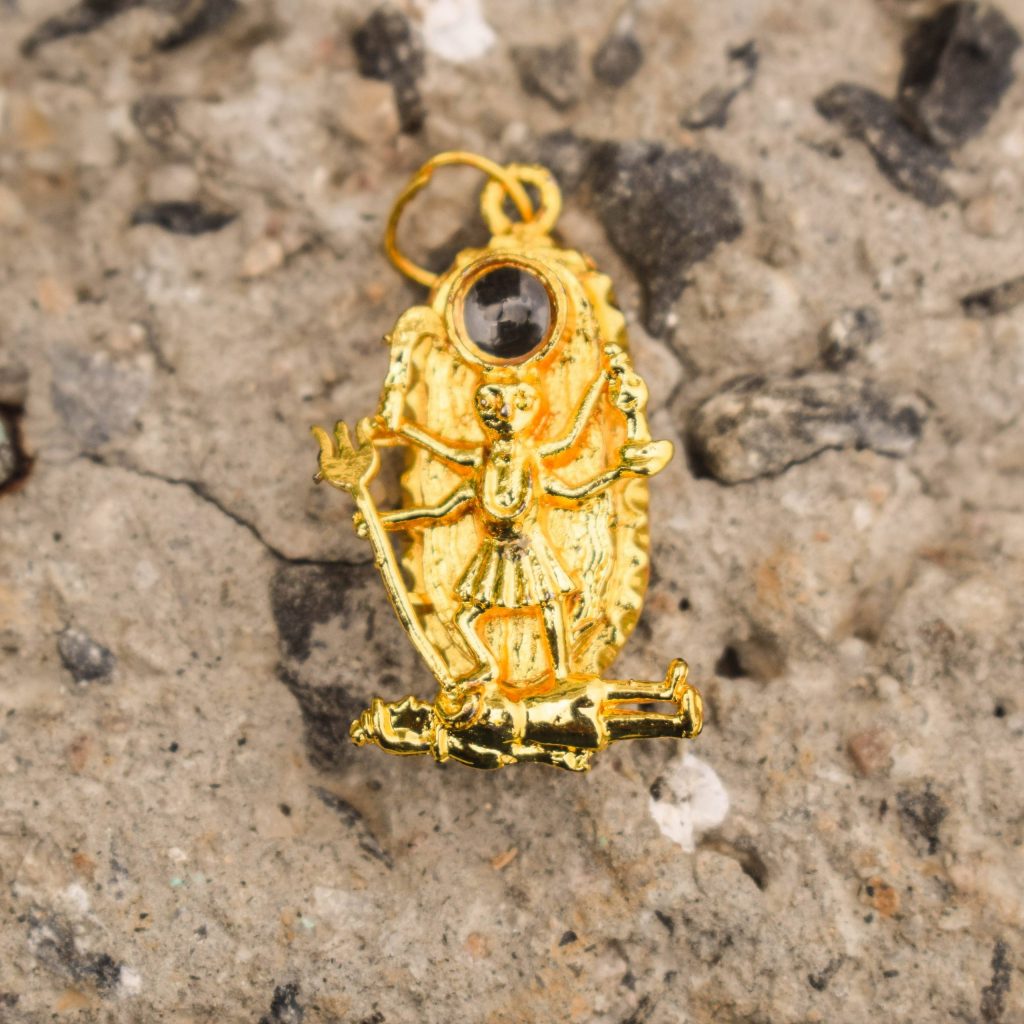 kali Kavach locket with golden chain placed on beech stone as shown in this image