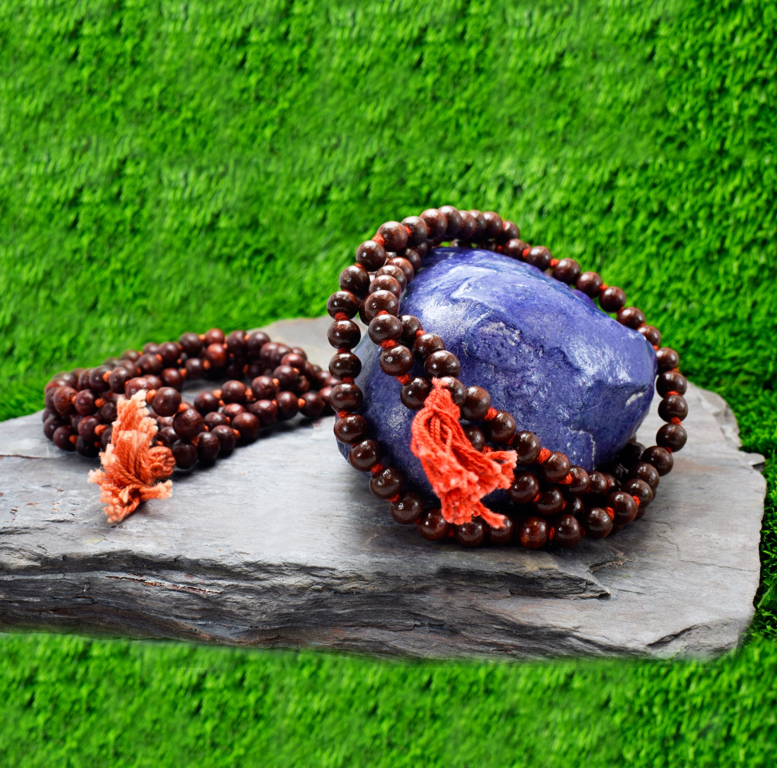 Two beautiful worship's mala of dark red color sandalwood MALA placed on a rock in front of green blur background.